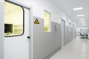 Flur in einem Krankenhaus. Eine Strahlenschutztür mit Fenster aus gelben Bleiglas ermöglicht den Blick in den Röntgen-Raum.