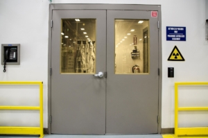 Zweiflügelige, graue Strahlenschutztür mit 2 Fenstern aus gelblichem Bleiglas.