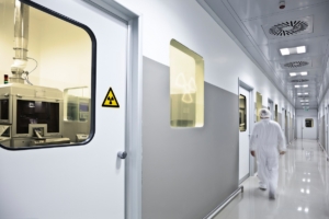 Flur in einer radiologischen Abteilung: Mehrere Strahlenschutztüren mit Fenster ermöglichen den Blick in die Labore. In einem der Bleifenster leuchtet dank LED-Technik ein Strahlungs-Warnsymbol.